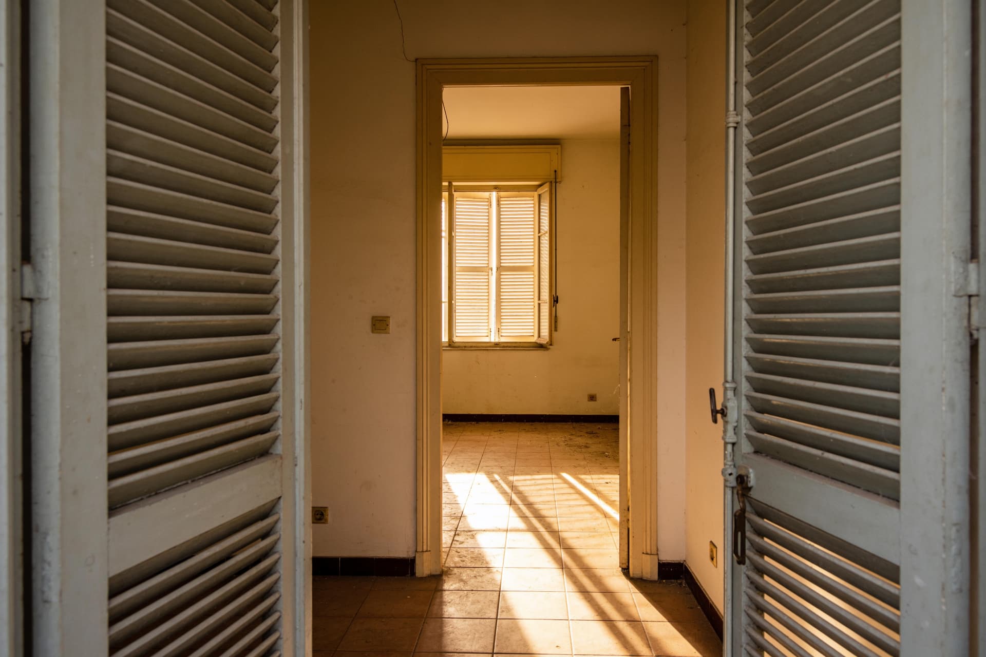 Appartement vide aux volets entrouverts baigné de lumière