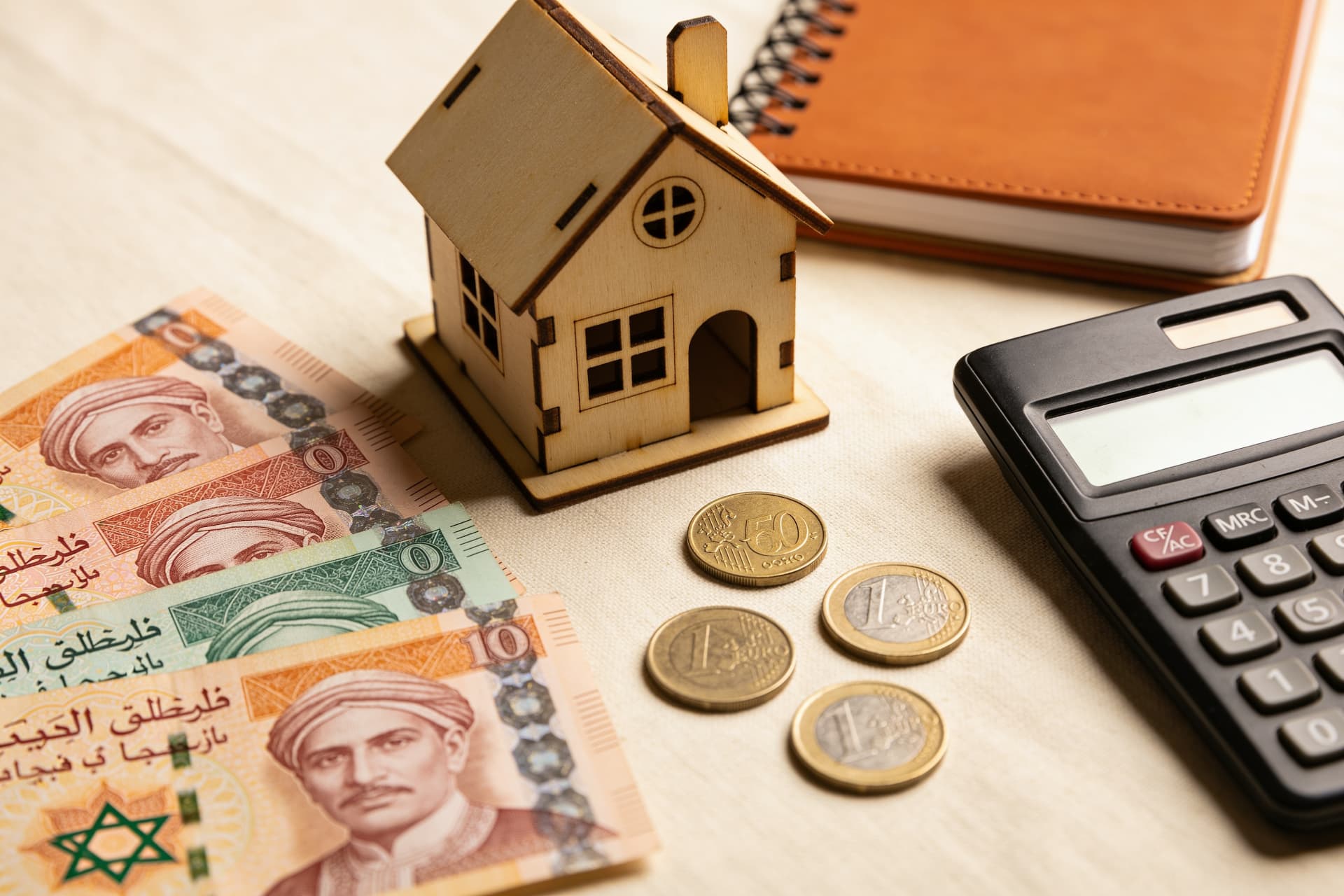 Billets de dirhams, maison miniature en bois et calculatrice posés sur une table